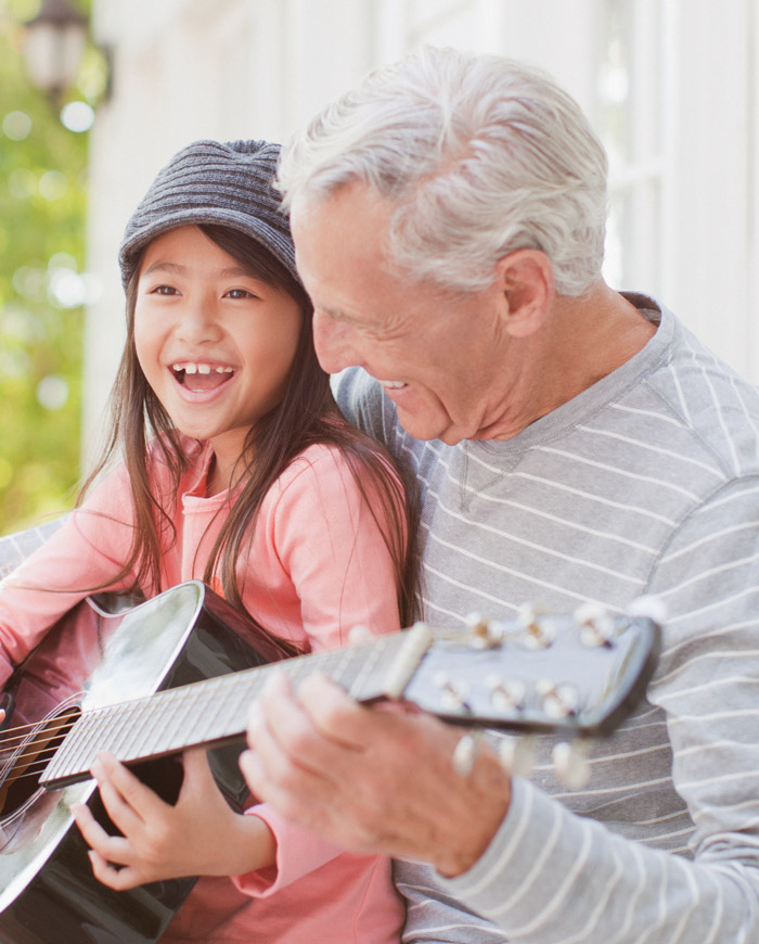 an older man plays guitar with his granddaughter